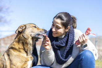 Portrait of a happy young woman giving a snack to her dog in the street