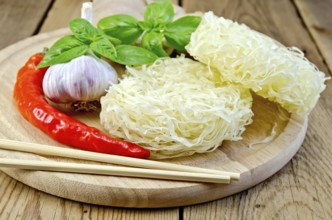 Stranded rice noodles with garlic, hot red pepper, ginger, basil, chopsticks on a wooden boards