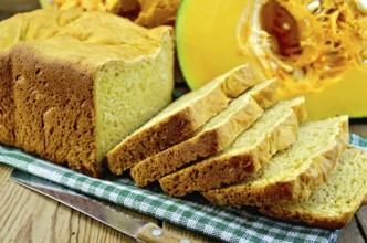 Homemade pumpkin bread on a green napkin, cut pumpkin, knife on background wooden board