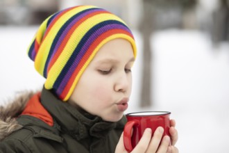 Glückliches Kind Kind Teenager Junge hält roten Becher mit heißem Kakao, Schokolade oder Tee und