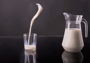 Glass jug and cup filled with white milk. Pouring organic drink in motion