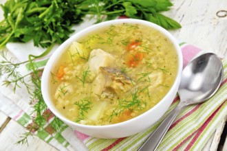 Soup fish kulesh with millet, potatoes and carrots in a white bowl on a napkin, parsley, dill on a