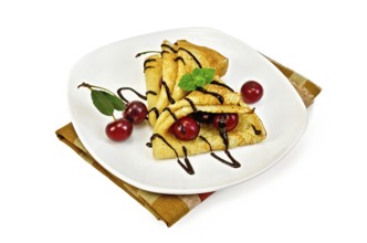Two pancakes with berries cherries, mint, chocolate icing on a white plate and napkin isolated on