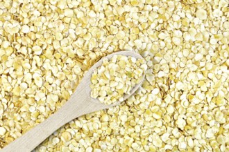 Texture of yellow pea flakes with a wooden spoon
