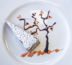 A typical italian slice of cake caprese made of chocolate and almonds with decorative tree made of