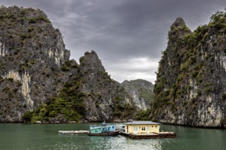 Single houseboat between towering limestone cliffs under a grey sky, The floating villages in