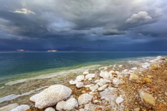 Rocky beach covered with evaporated salt. The Dead Sea is a closed salt lake. Gloomy sky with dark