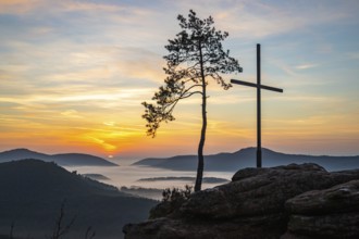 Landscape shot of nature in the morning. Mist in the valley and a summit cross on a sandstone cliff