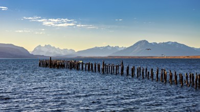 A peaceful coastal landscape with mountains in the background and an old wooden jetty in the sea,