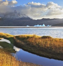 Gray lake and snow-capped mountains. Blue iceberg floating in the distance. Warm summer sunset
