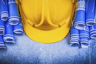 Blue rolled engineering drawings yellow building helmet on metallic background construction concept