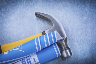 Blue rolled blueprints claw hammer on metallic background construction concept