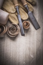 Wooden mallet curled up shavings flat chisels leather gloves on wood board vertical view