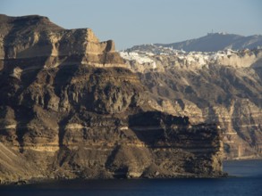 A wide mountain panorama with a sea and rocks in the foreground and a village in the background,