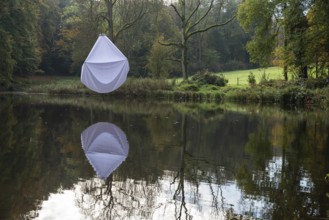 Reflecting water pond in a park with a white bed sheet hanging in a tree
