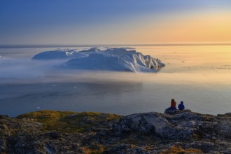 Large glaciers in the bay by the rocky shore in the light of the setting sun with fog over the