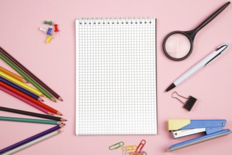 Colored pencils, stationery, paper notebook with pen and magnifier on pink isolated background. top