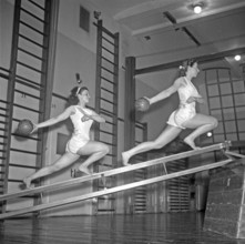 Gymnastics in the 1940s. Two young women are balancing on gymnasium equipment and at the same time