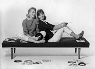 1960s lifestyle. Two girls in typical 1960s clothes are sitting together holding music records.