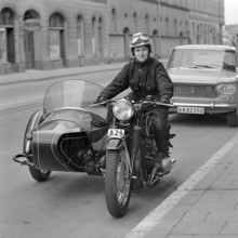 In the 1960s. A woman seen dressed in the typical motorcycle drivers outfit and helmet at her