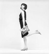 In the 1960s. A model in a typical 1960s outfit photographed in a studio. A black popular dress in
