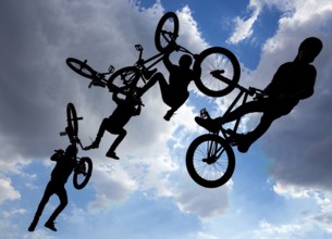 An extreme rider is making a free style jump from a ramp. The young boy with his bicycle is seen as