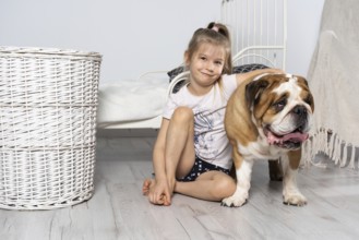 A young girl in a bedroom, sitting on the floor with her dog and stroking him. Child and dog. The