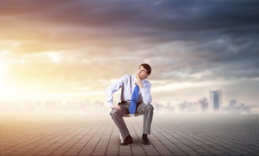Young businessman sits on an office chair, thoughtful and looking up