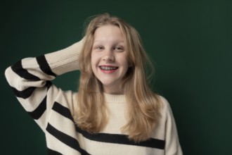 A woman with blonde hair is standing, wearing a striped sweater. She appears calm and is looking