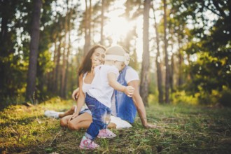 Young parents are taught to walk a daughter of one year on nature in a park on a lawn. The first