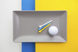 Gray ceramic dish with golf equipments on over white, blue and yellow wooden table, rectangle dish