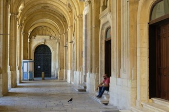A man with his sandwich and two hungry pigeons in the archway of the National Library, Valletta,