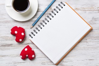 Coffee cup notepad pencil and two red hearts on wooden surface