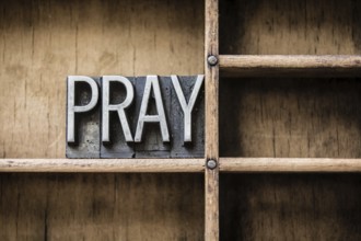 The word PRAY written in vintage letterpress type sitting in a wooden drawer