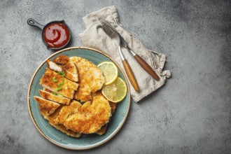 Crispy panko breaded fried chicken fillet with green salad and lemon cut on plate on gray