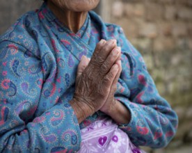 Unrecognized elder nepalise woman wearing blue cloths crossing her wrinkled hands