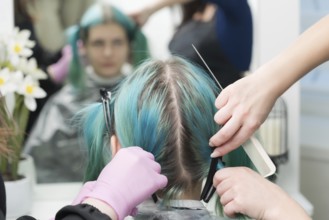 Back view of female head with emerald hair color and regrown hair roots. Woman sits in chair by