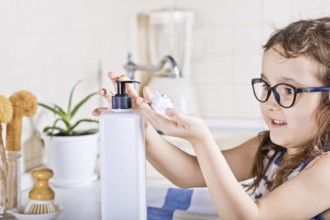 Little kid child washing hands with soap dispenser in a kitchen. Mock-up white container