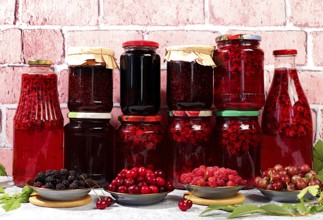 Jars with raspberry, cherry, gooseberry jam and compote on kitchen background with leaves and fresh