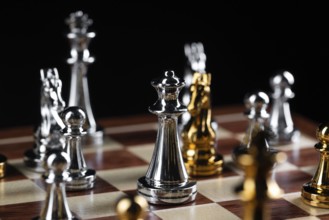 Gold and silver chess figures placed on wooden chessboard. Intellectual duel and tactical battle in