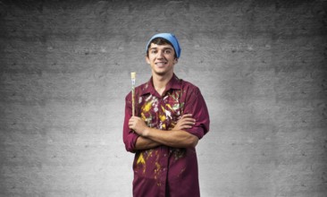Young happy painter artist holding paintbrush. Portrait of painter in dirty shirt and bandana