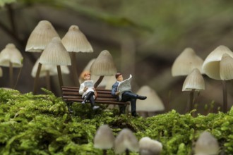 Small figures reading the newspaper and resting under the fungus mycena arcangeliana in the forest