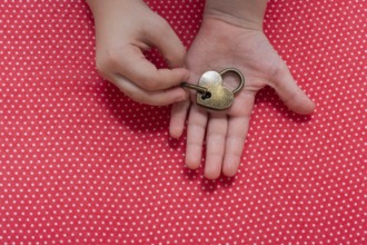 Hand holding a heart shaped lock and key on a red background