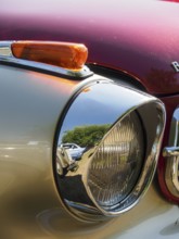 Close-up of a chrome-plated spotlight with reflection of the surroundings on a red background,