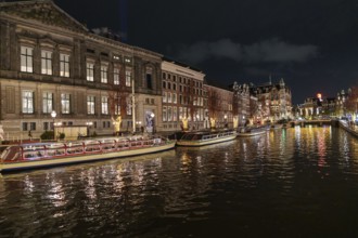 Illuminated boats and buildings are reflected in the canal water at night, Amsterdam, Netherlands