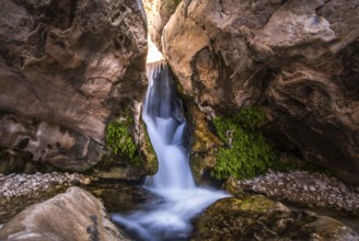Small waterfall flows through a rocky gorge with moss, Oman
