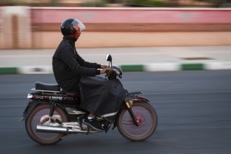 Marrakesh, MOROCCO - OCTOBER 5, 2024: Moroccan man riding a scooter on the road. Blurred background