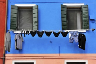 Venice, Veneto, Italy, Europe, Vibrant blue façade with green shutters, contrasting clothing on