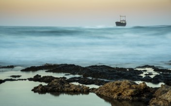 Abandoned ship in the stormy sea with big wind waves during sunset