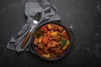 Beef meat stew with potatoes, carrot and delicious gravy in black casserole pot with bay leaves